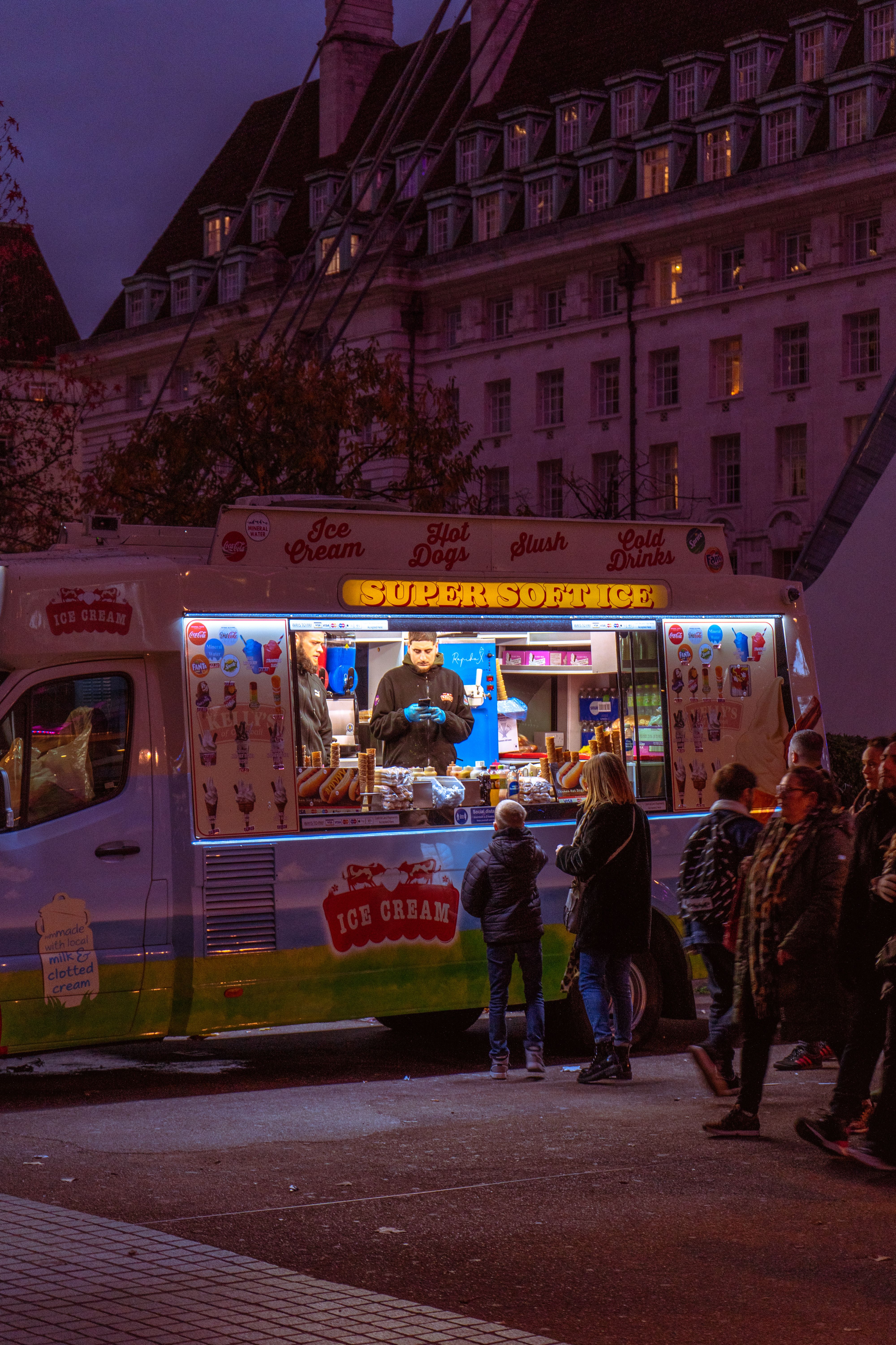 Un food truck de glaces et hot-dogs, vitrine illuminée en soirée, avec des clients devant